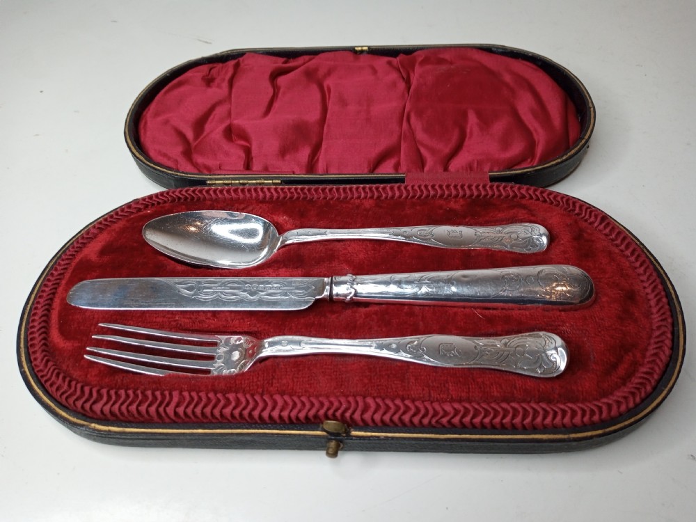 An antique three-piece silver christening cutlery set housed within a open red velvet-lined presentation case.