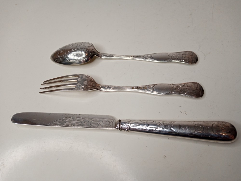 An antique three-piece silver christening cutlery set housed within a open red velvet-lined presentation case. View V