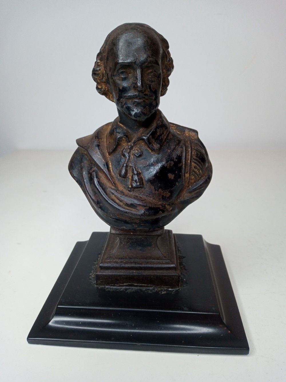 A dark metal portrait bust of William Shakespeare mounted on a square black marble plinth.