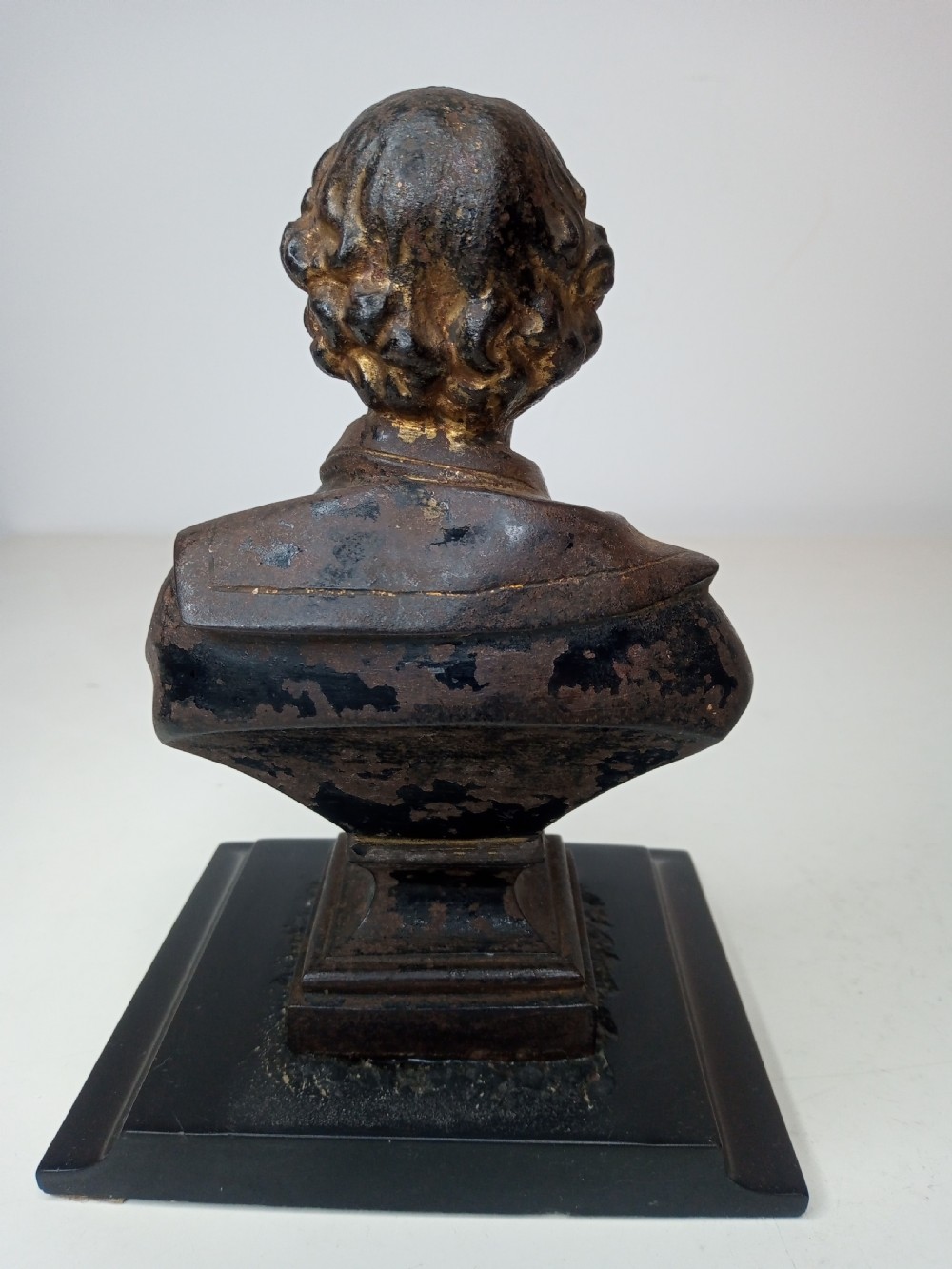 A dark metal portrait bust of William Shakespeare mounted on a square black marble plinth. View II