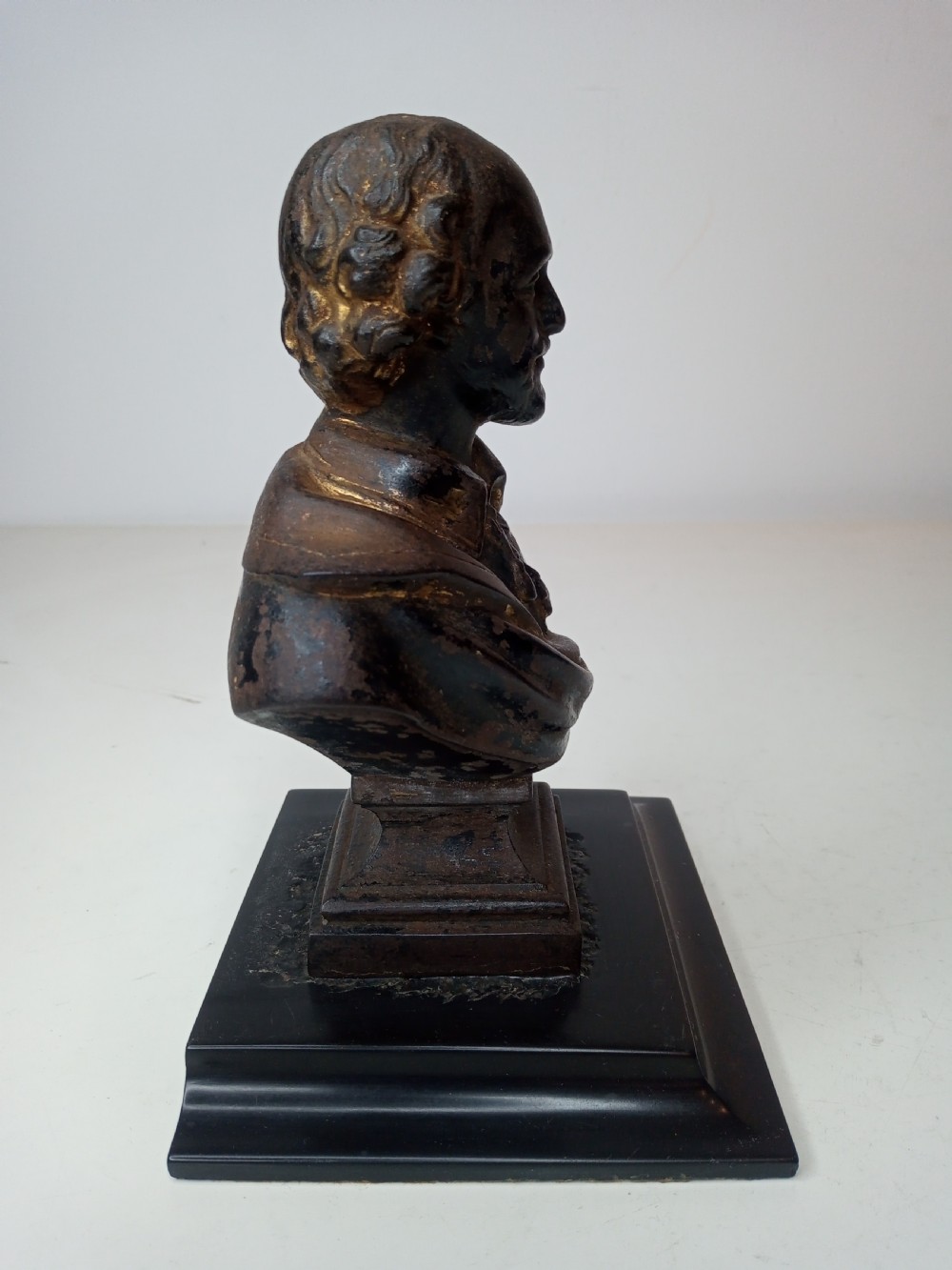 A dark metal portrait bust of William Shakespeare mounted on a square black marble plinth. View IV