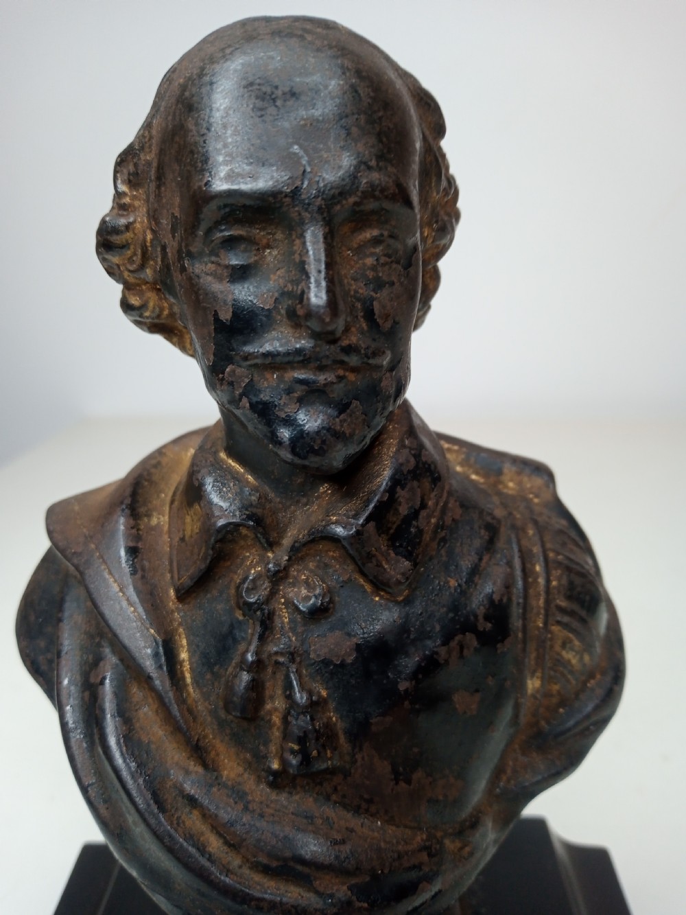 A dark metal portrait bust of William Shakespeare mounted on a square black marble plinth. View V