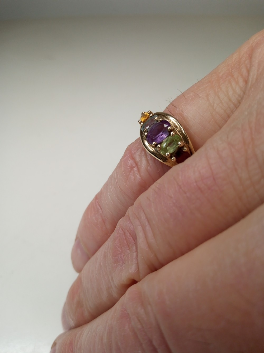 A nine-carat yellow gold ring featuring a horizontal row of five oval gemstones in varied colours within a boat-shaped mount. View VI