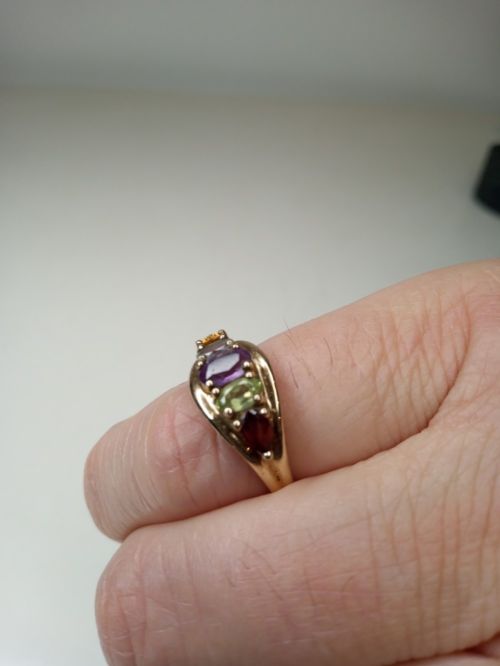 A nine-carat yellow gold ring featuring a horizontal row of five oval gemstones in varied colours within a boat-shaped mount. View VII