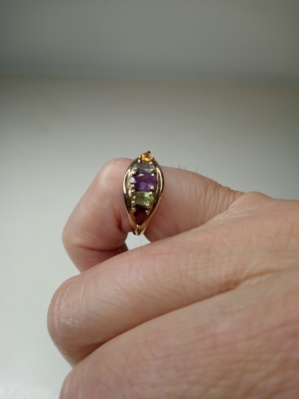 A nine-carat yellow gold ring featuring a horizontal row of five oval gemstones in varied colours within a boat-shaped mount. View VIII