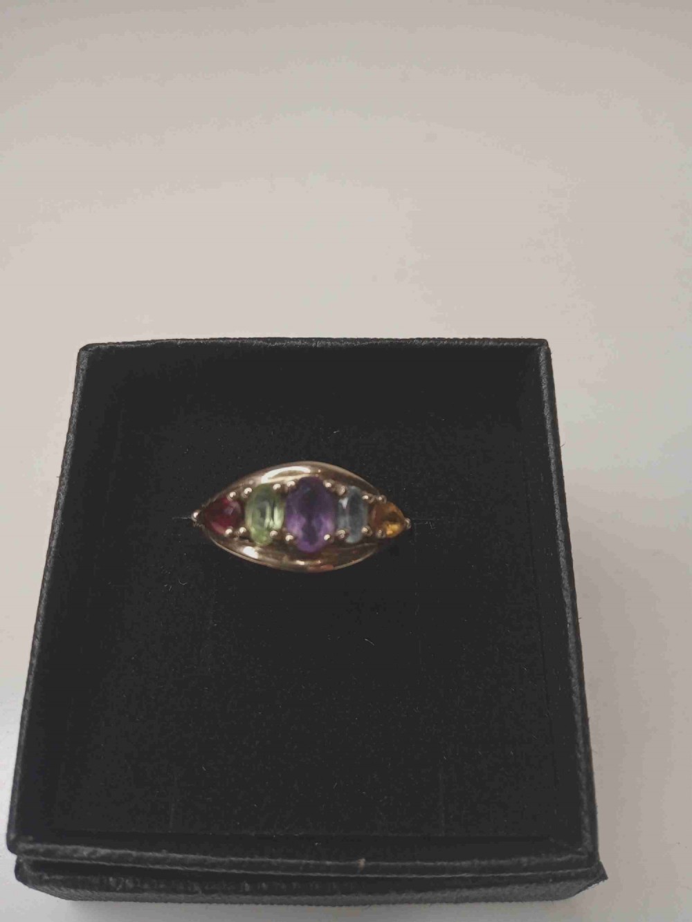 A nine-carat yellow gold ring featuring a horizontal row of five oval gemstones in varied colours within a boat-shaped mount.