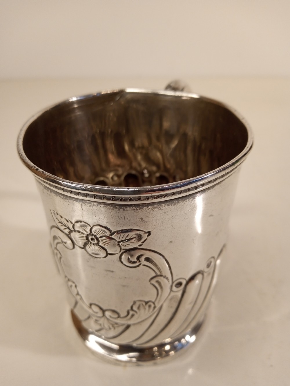 A sterling silver tankard with chased floral decoration and scroll cartouche detailing on a polished surface.