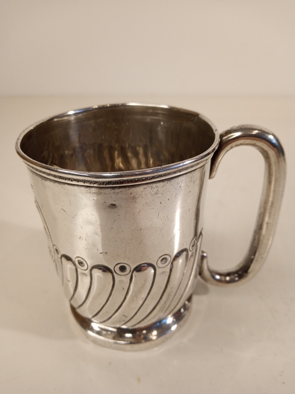 A sterling silver tankard with chased floral decoration and scroll cartouche detailing on a polished surface. View II