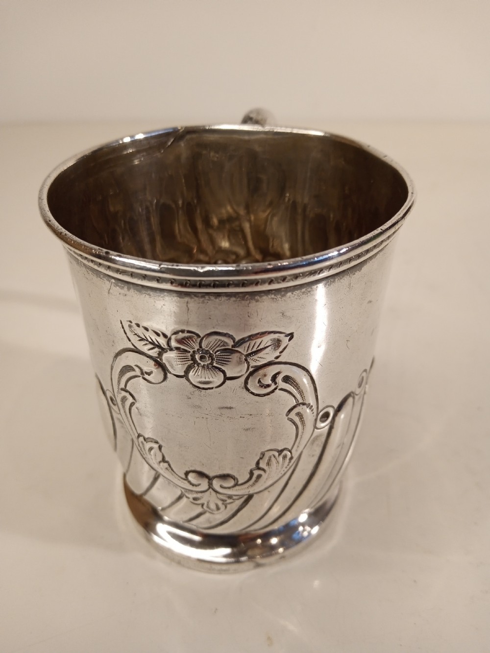 A sterling silver tankard with chased floral decoration and scroll cartouche detailing on a polished surface. View V