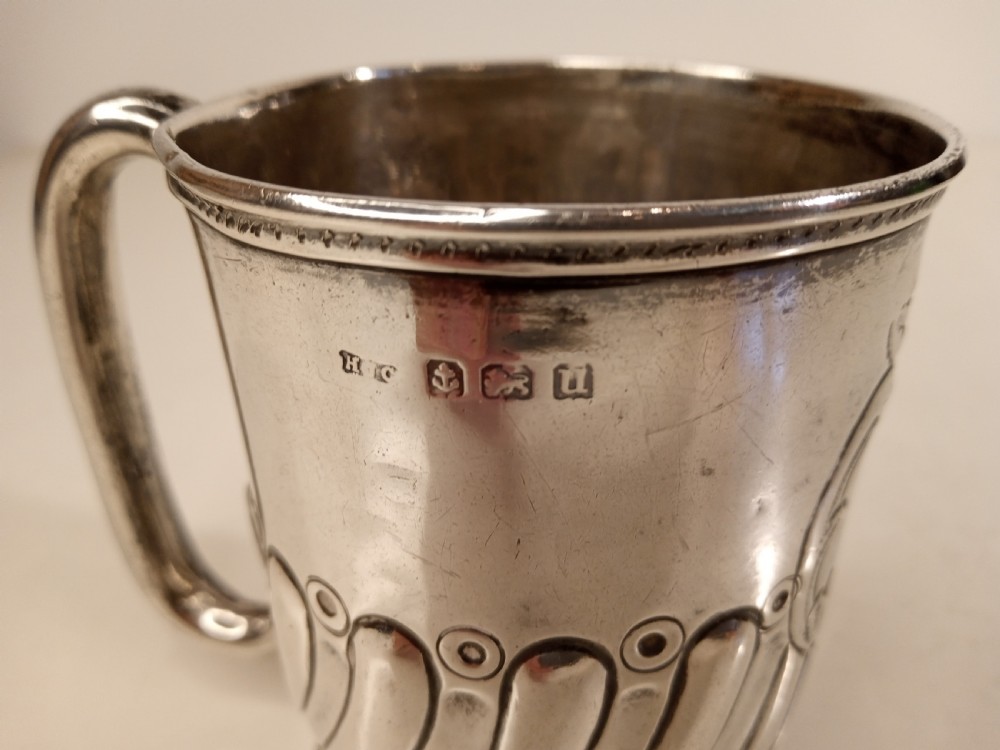 A sterling silver tankard with chased floral decoration and scroll cartouche detailing on a polished surface. View VI