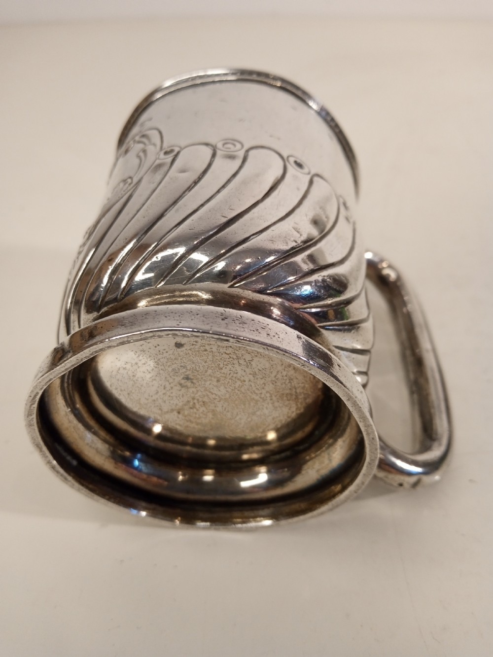 A sterling silver tankard with chased floral decoration and scroll cartouche detailing on a polished surface. View VII