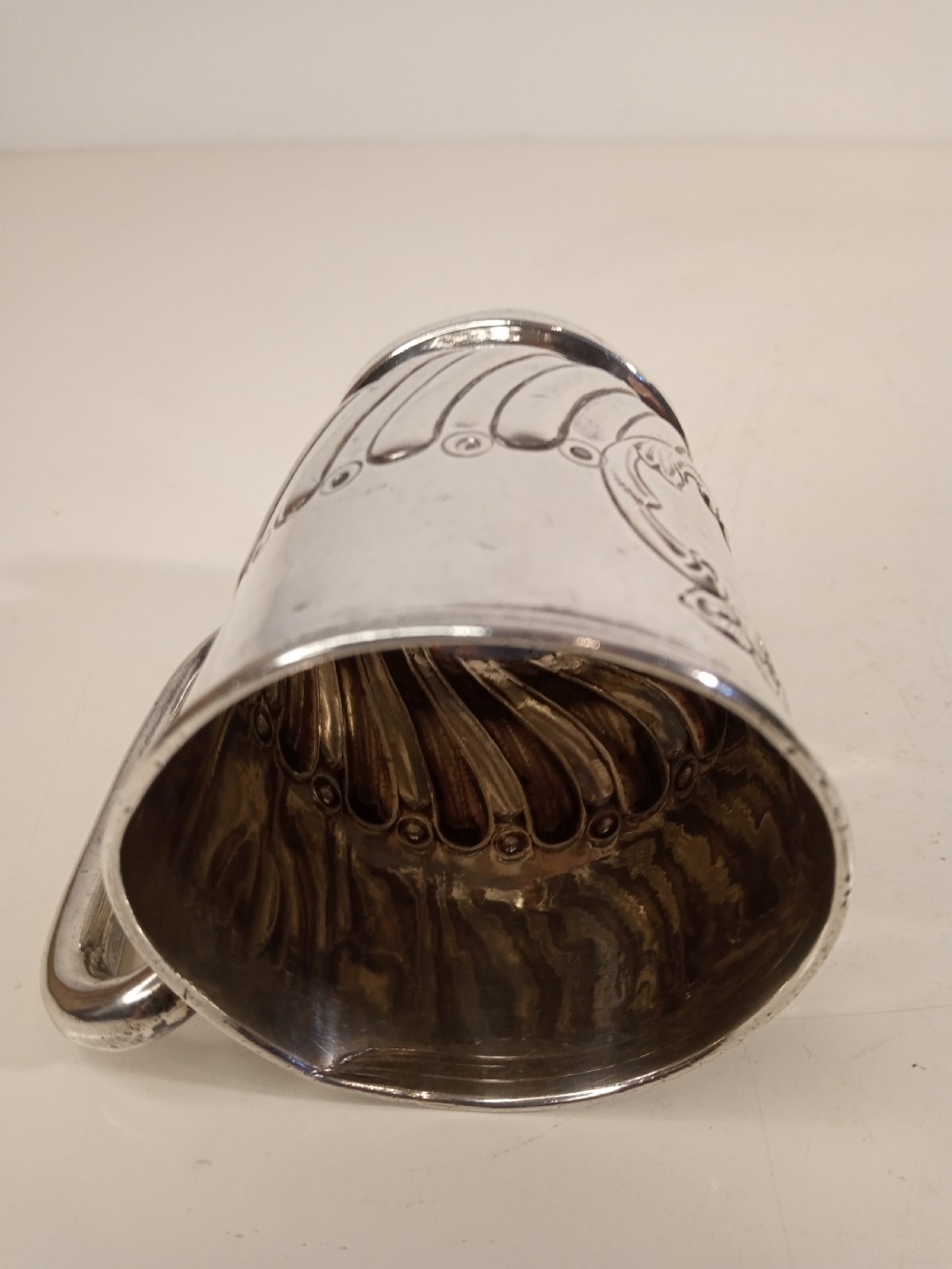 A sterling silver tankard with chased floral decoration and scroll cartouche detailing on a polished surface. View VIII