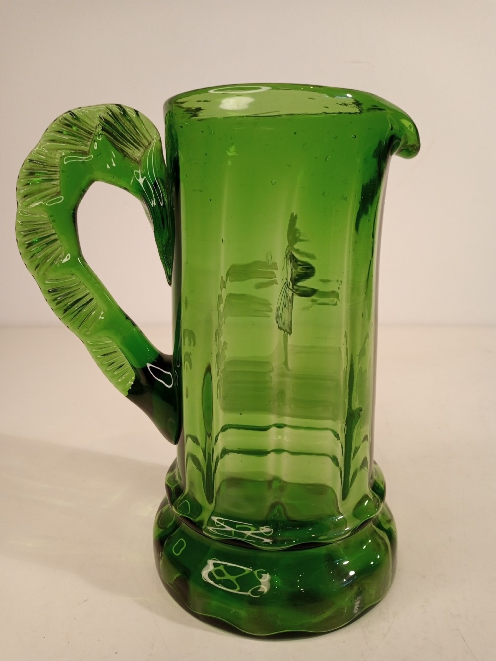 A Victorian emerald green glass pitcher featuring white enamel painting of a child figure among foliage, complete with a textured applied handle. View II