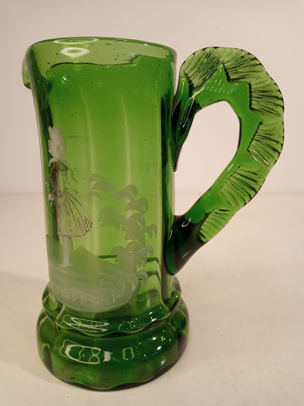 A Victorian emerald green glass pitcher featuring white enamel painting of a child figure among foliage, complete with a textured applied handle. View III