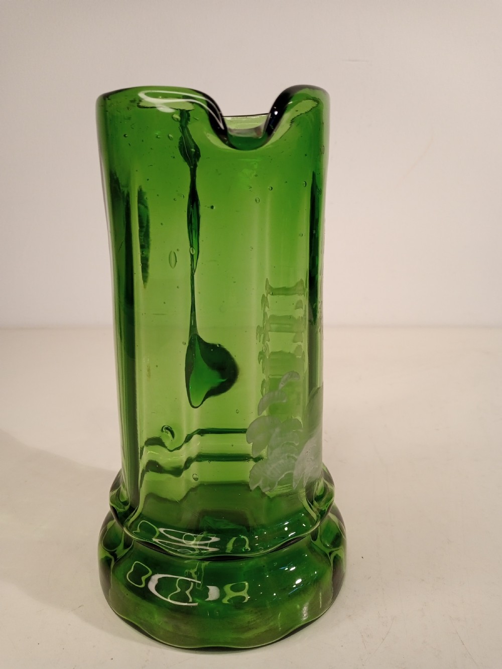 A Victorian emerald green glass pitcher featuring white enamel painting of a child figure among foliage, complete with a textured applied handle. View IV