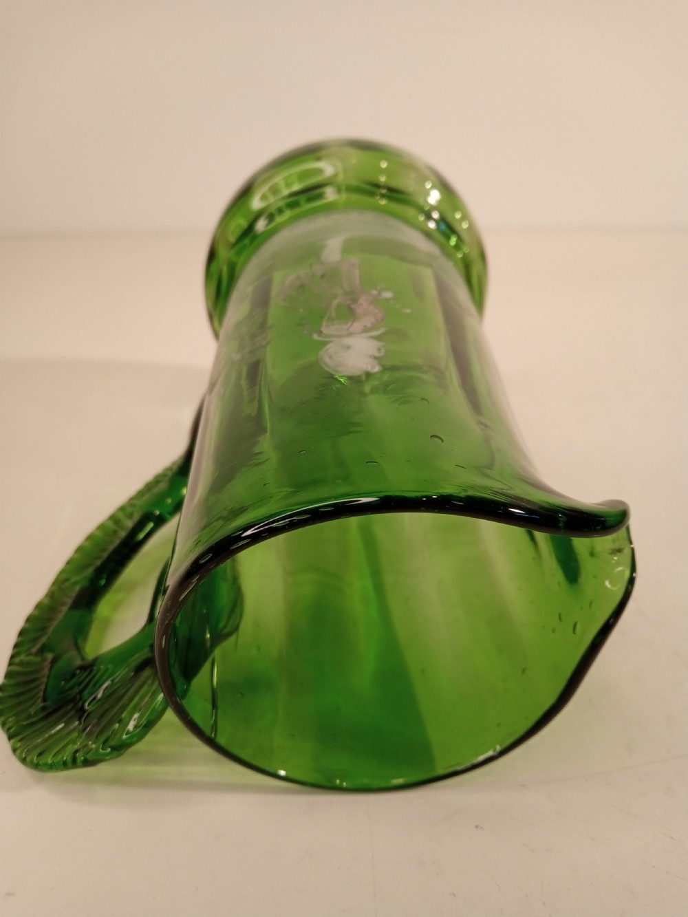 A Victorian emerald green glass pitcher featuring white enamel painting of a child figure among foliage, complete with a textured applied handle. View VI