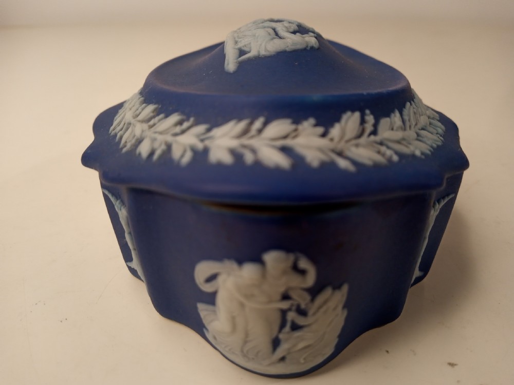 A dark blue oval jasperware lidded box featuring raised white classical bas-relief figures on the top surrounded by a white laurel leaf border. View VIII