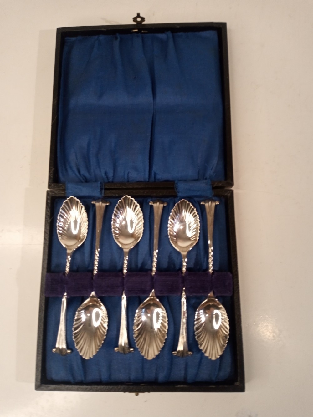 A boxed set of six late nineteenth-century sterling silver coffee spoons with fluted shell-shaped bowls set against a blue fabric lining.