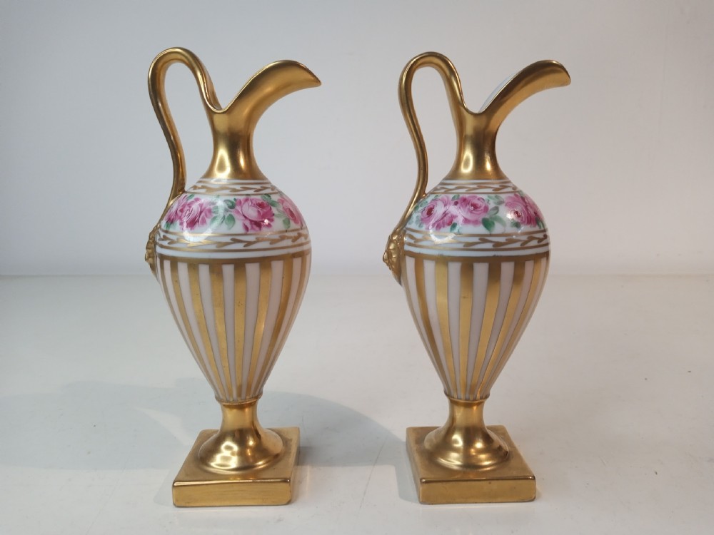 A pair of antique porcelain ewer vases featuring gilded spouts, vertical stripes, square pedestal bases, and hand-painted pink rose garlands around the shoulders. View III