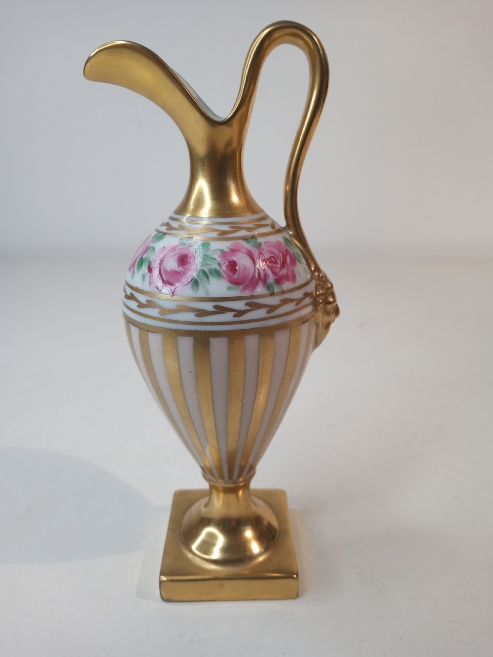 A pair of antique porcelain ewer vases featuring gilded spouts, vertical stripes, square pedestal bases, and hand-painted pink rose garlands around the shoulders. View V