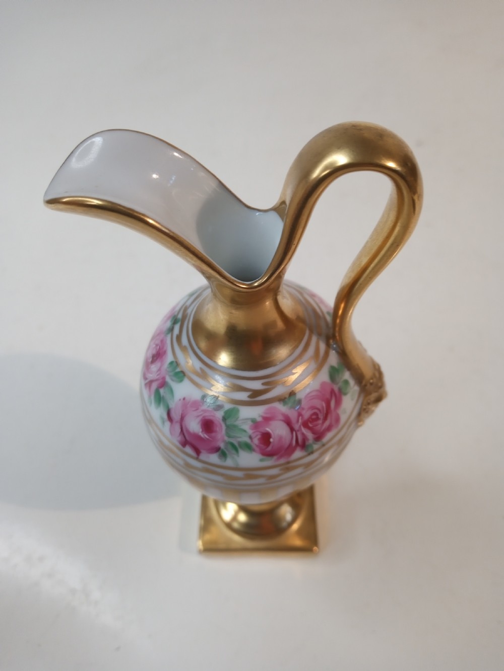 A pair of antique porcelain ewer vases featuring gilded spouts, vertical stripes, square pedestal bases, and hand-painted pink rose garlands around the shoulders. View VI
