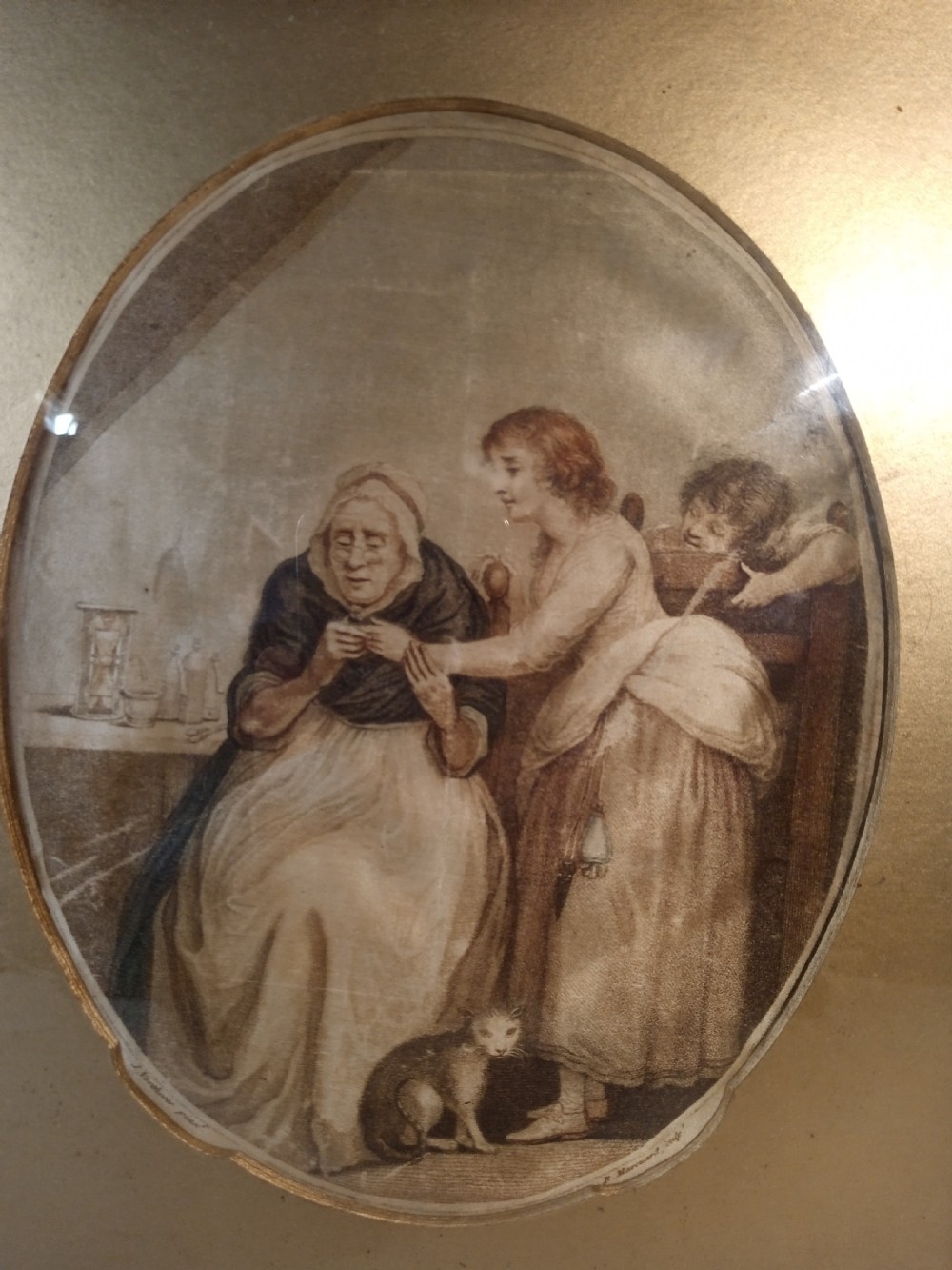 A late Georgian framed stipple engraving printed on silk depicting a domestic scene within an oval vignette, set inside a gilded wooden frame. View II