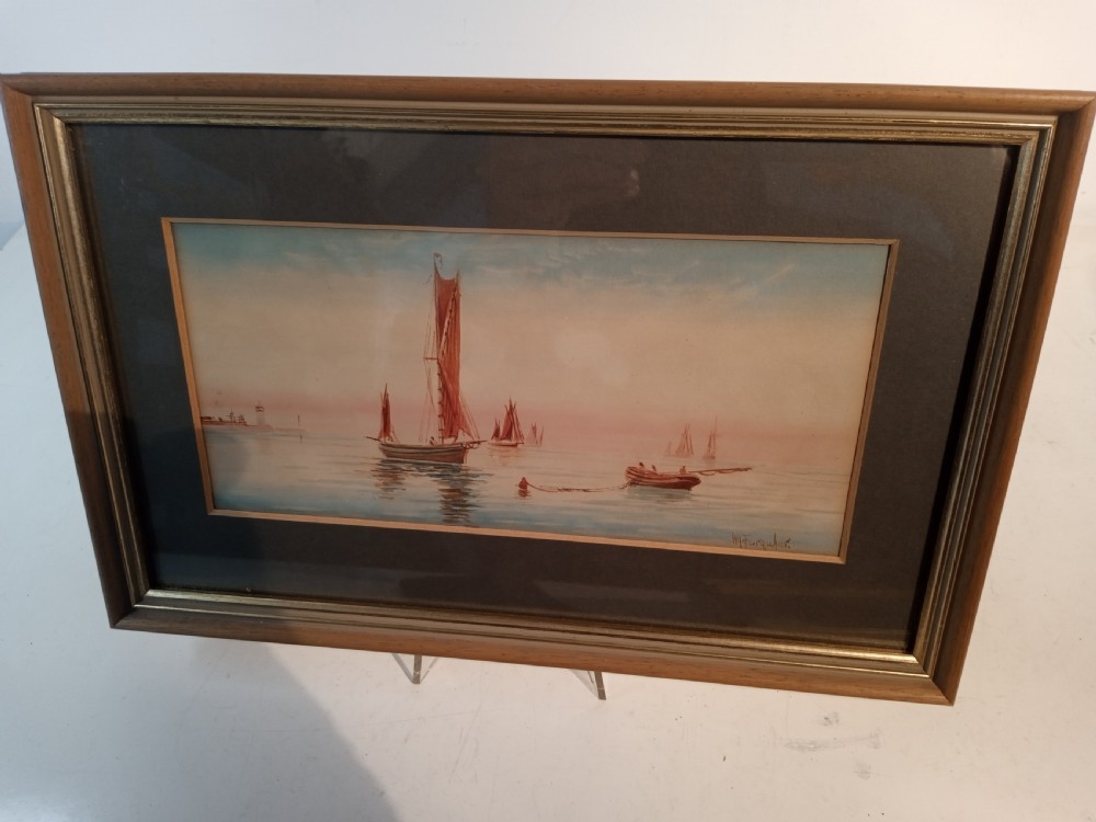 A horizontal nineteenth-century Victorian watercolour painting depicting reddish-brown sailing vessels on calm blue water with a distant lighthouse, housed in a double mount and wooden frame.