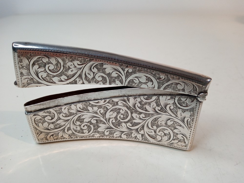 An Edwardian sterling silver card case featuring detailed foliage engraving across a gently curved rectangular body with a hinged cap.