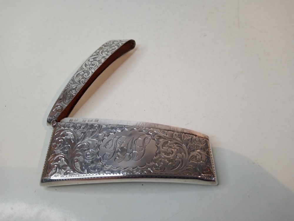 An Edwardian sterling silver card case featuring detailed foliage engraving across a gently curved rectangular body with a hinged cap. View IV