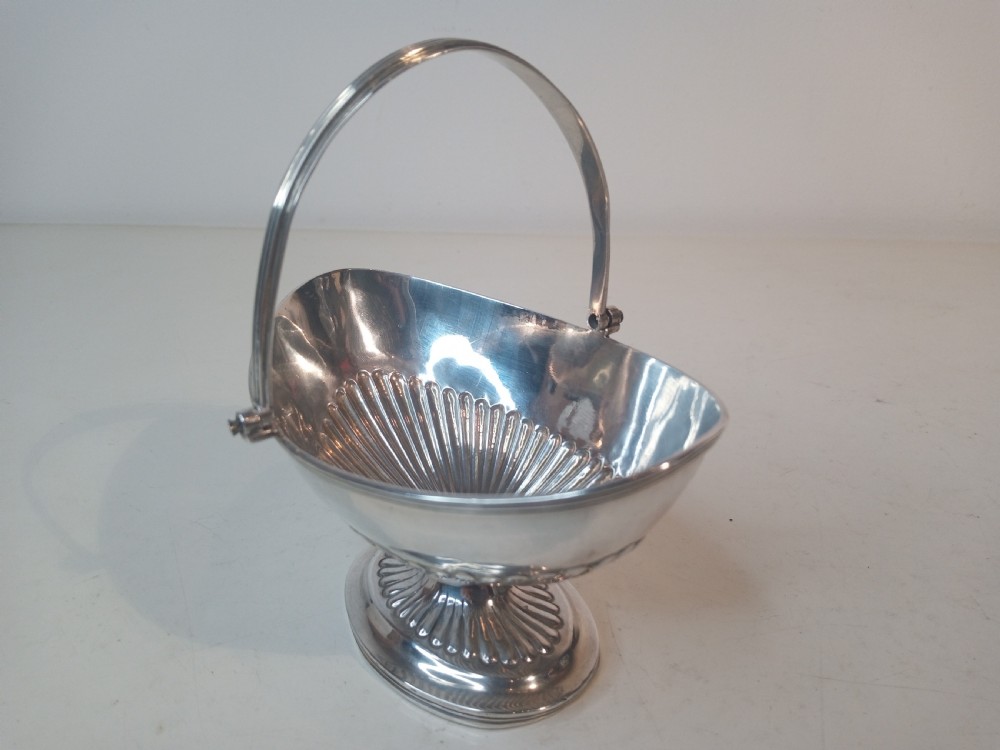A Victorian sterling silver sweet basket featuring a pedestal foot, fluted detailing, and an upright swing handle. View II