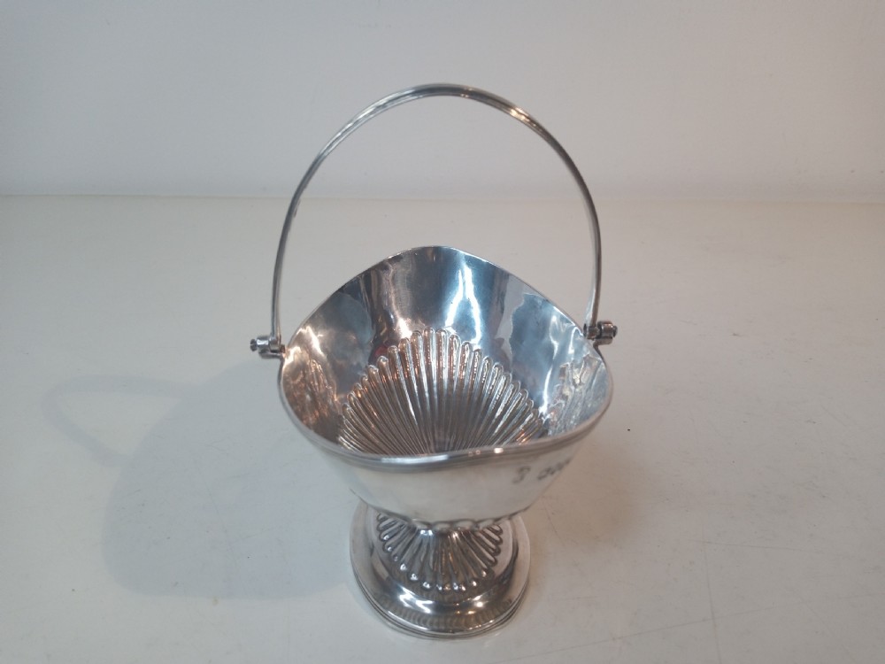 A Victorian sterling silver sweet basket featuring a pedestal foot, fluted detailing, and an upright swing handle. View III