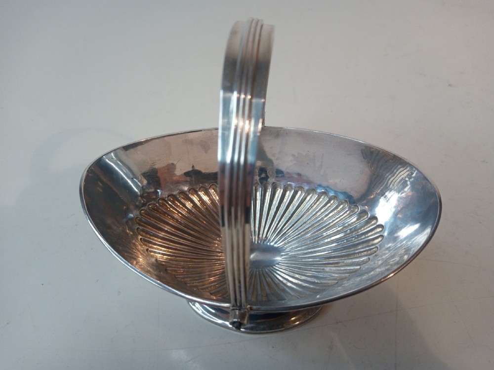 A Victorian sterling silver sweet basket featuring a pedestal foot, fluted detailing, and an upright swing handle. View IV