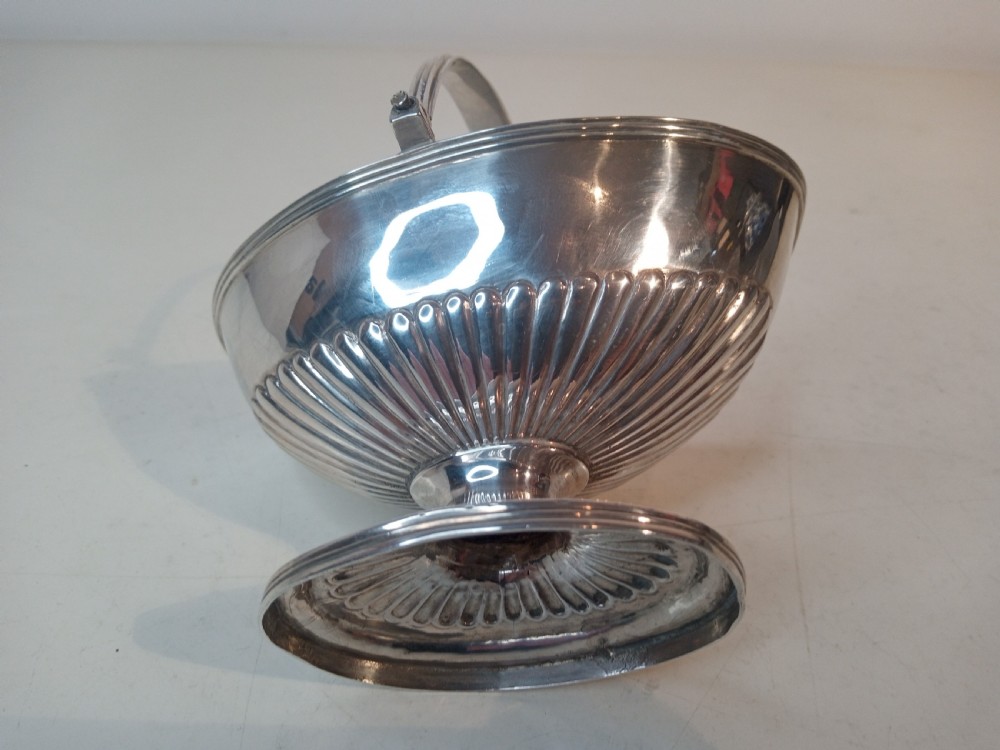A Victorian sterling silver sweet basket featuring a pedestal foot, fluted detailing, and an upright swing handle. View V