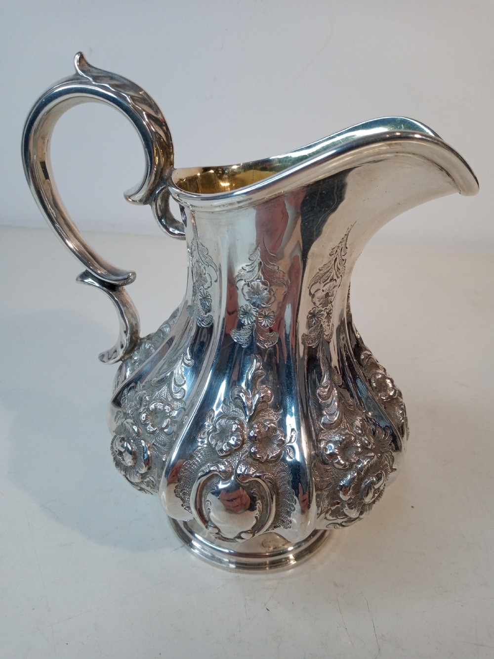 A Victorian sterling silver jug featuring hand-chased floral patterns, a fluted lower body, a scroll handle, and a gilt interior. View III