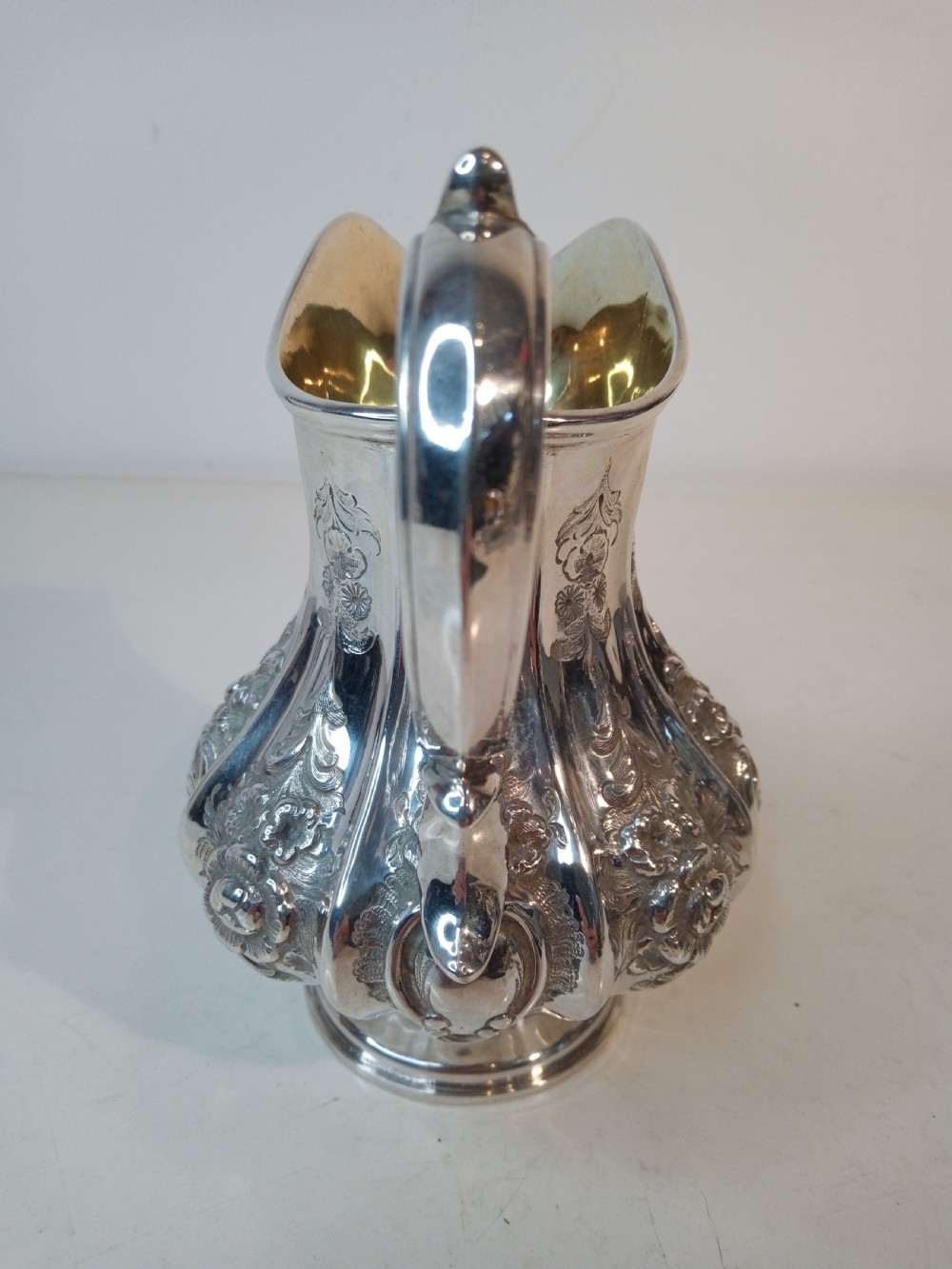 A Victorian sterling silver jug featuring hand-chased floral patterns, a fluted lower body, a scroll handle, and a gilt interior. View IV
