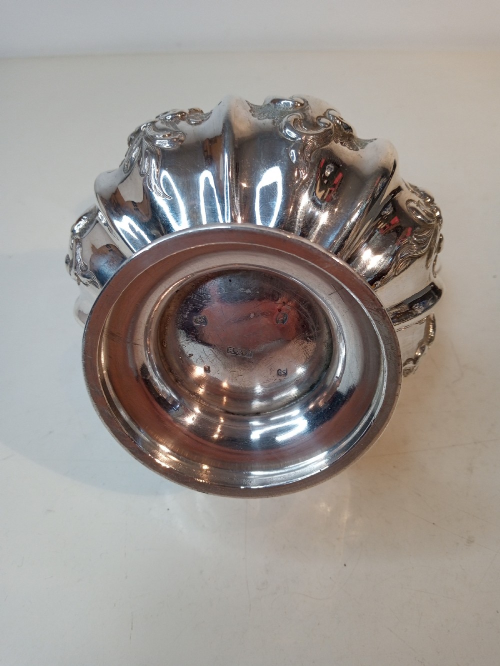 A Victorian sterling silver jug featuring hand-chased floral patterns, a fluted lower body, a scroll handle, and a gilt interior. View VI