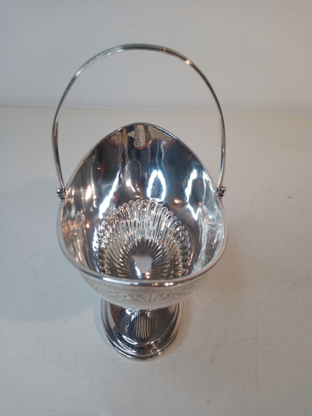 A Victorian sterling silver pedestal sweet basket featuring a reeded overhead handle, fluted interior base, and engraved decorative rim band. View II