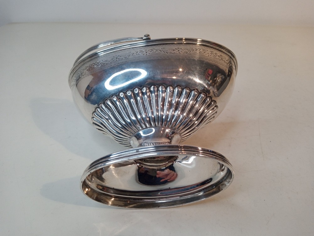 A Victorian sterling silver pedestal sweet basket featuring a reeded overhead handle, fluted interior base, and engraved decorative rim band. View IV