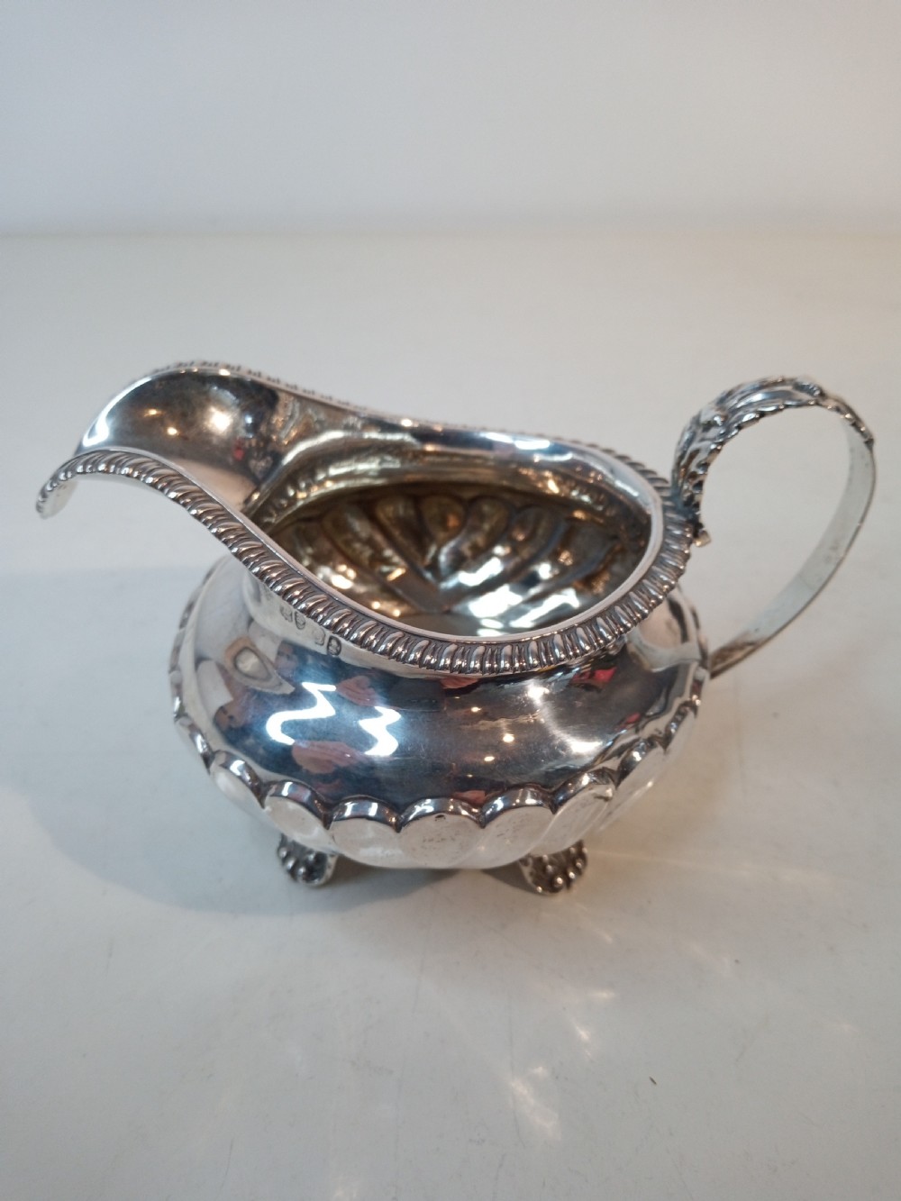 An antique Georgian sterling silver cream jug with a gadrooned rim, fluted lower body, cast handle, and four small feet.