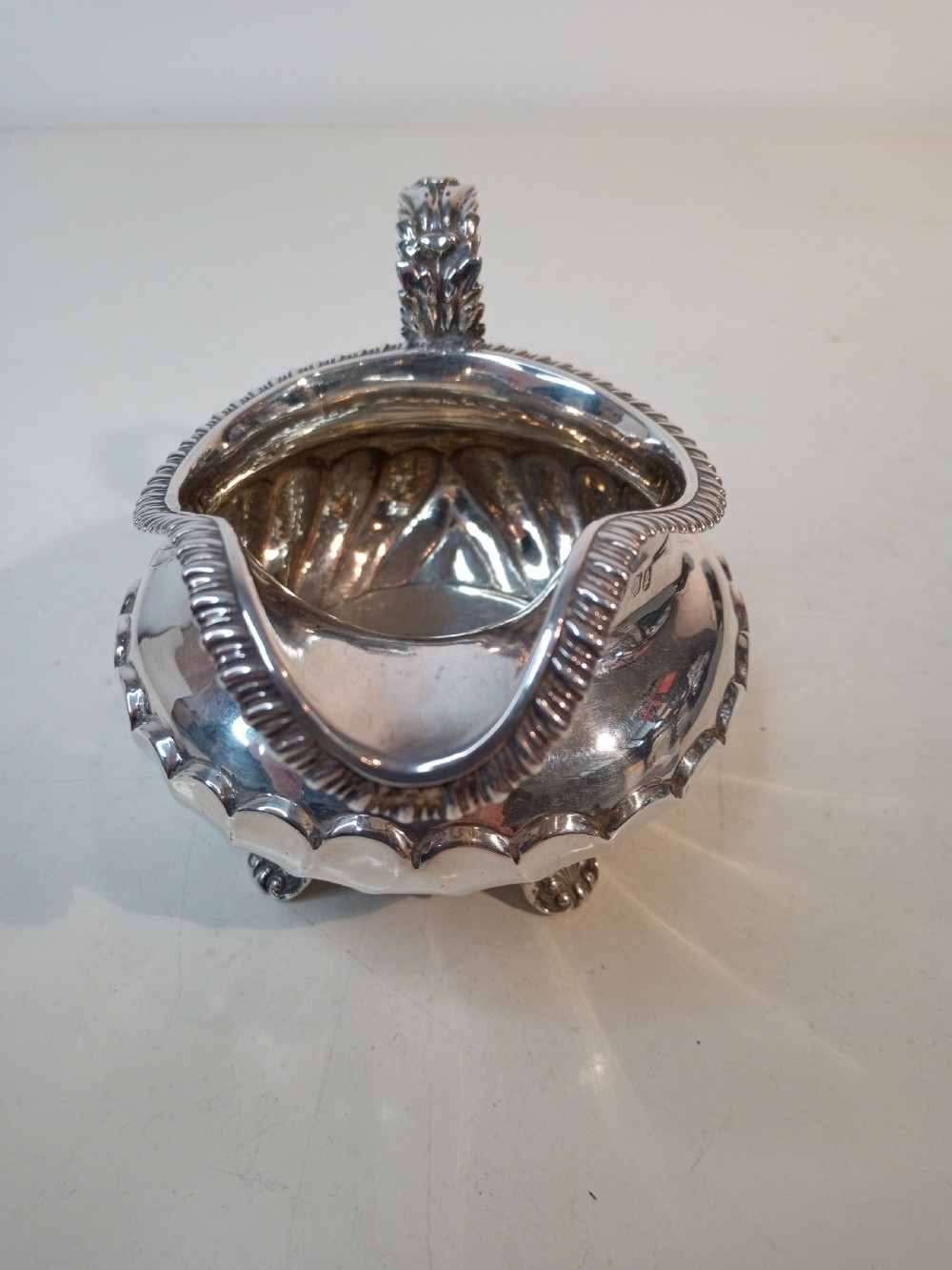 An antique Georgian sterling silver cream jug with a gadrooned rim, fluted lower body, cast handle, and four small feet. View II