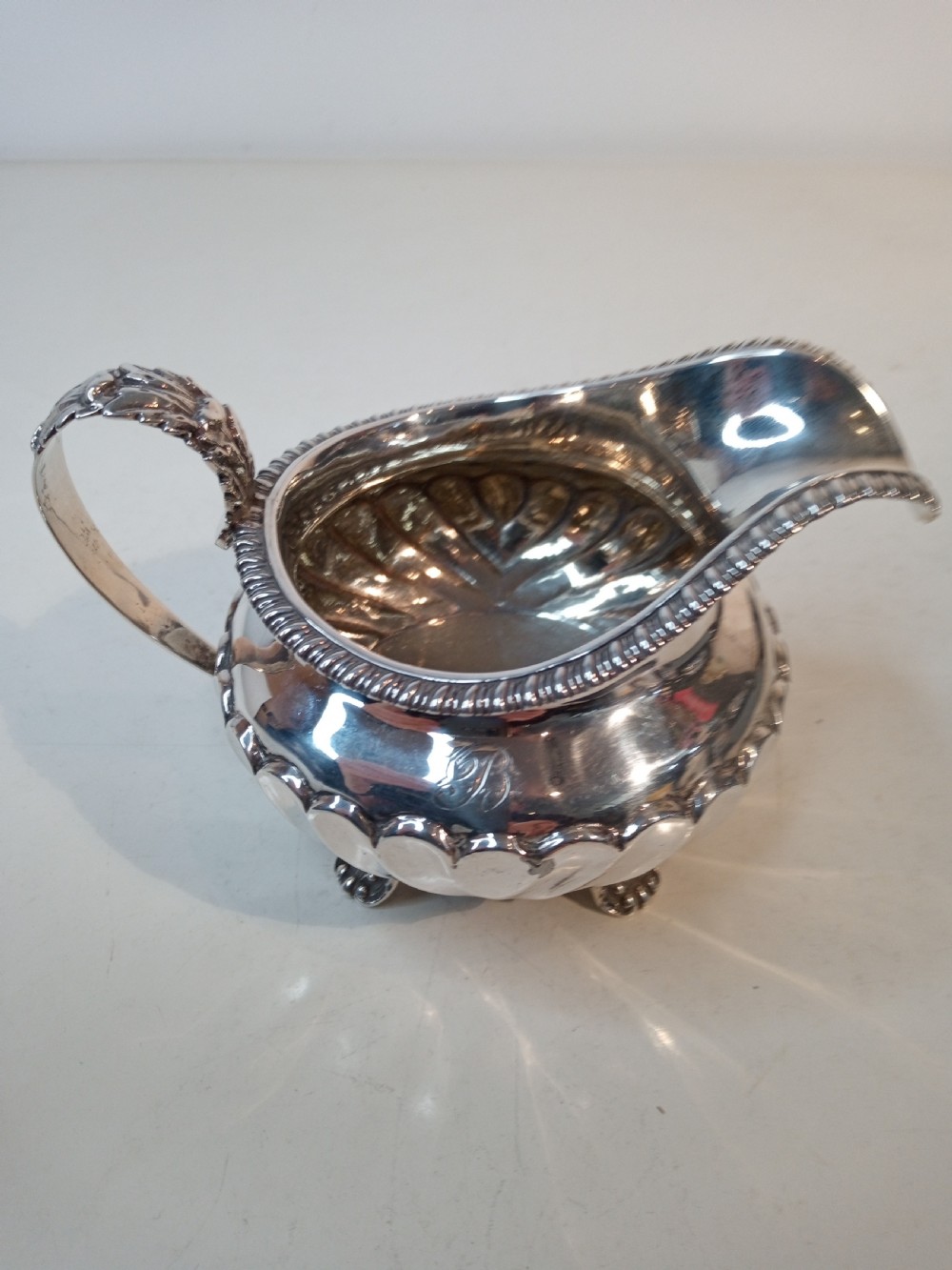An antique Georgian sterling silver cream jug with a gadrooned rim, fluted lower body, cast handle, and four small feet. View III
