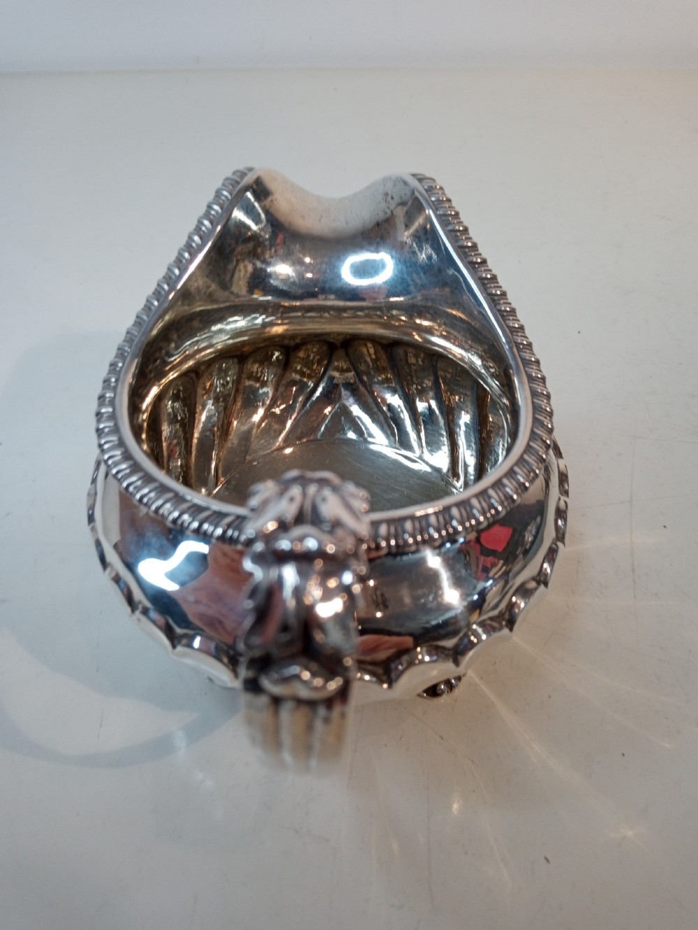 An antique Georgian sterling silver cream jug with a gadrooned rim, fluted lower body, cast handle, and four small feet. View IV