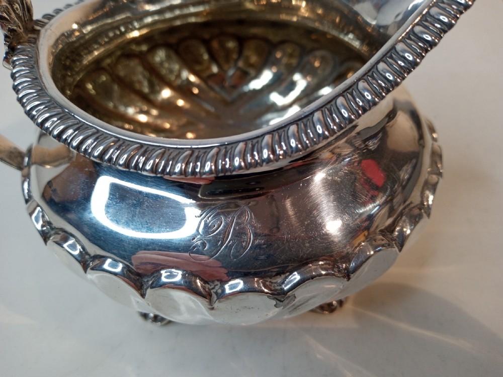 An antique Georgian sterling silver cream jug with a gadrooned rim, fluted lower body, cast handle, and four small feet. View VI