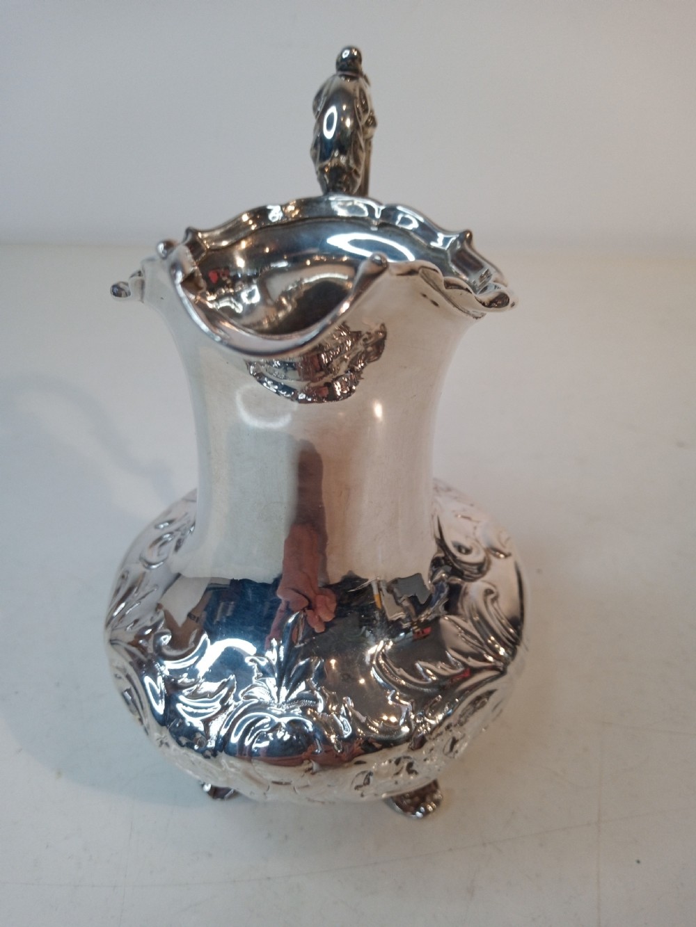 A Victorian hallmarked sterling silver jug with intricate scroll chasing, a shaped pour spout, a decorative handle, and scroll feet. View II