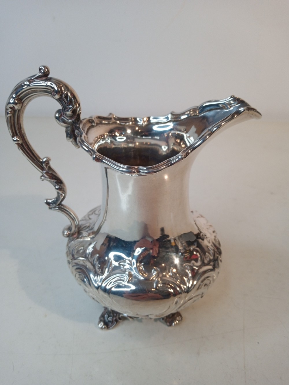 A Victorian hallmarked sterling silver jug with intricate scroll chasing, a shaped pour spout, a decorative handle, and scroll feet. View III