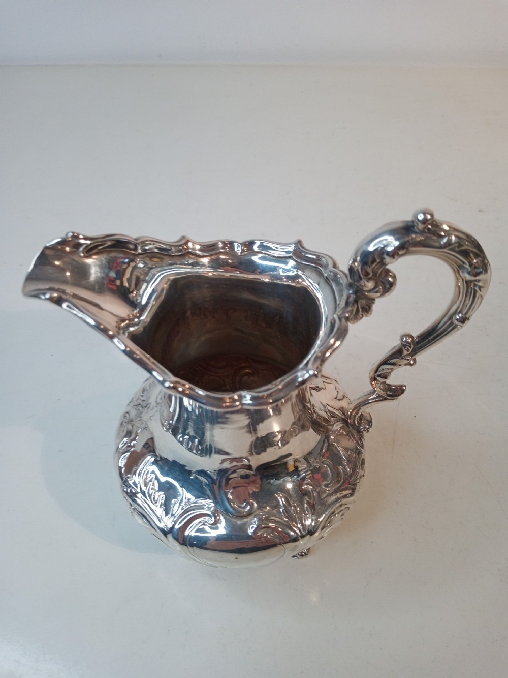 A Victorian hallmarked sterling silver jug with intricate scroll chasing, a shaped pour spout, a decorative handle, and scroll feet. View V