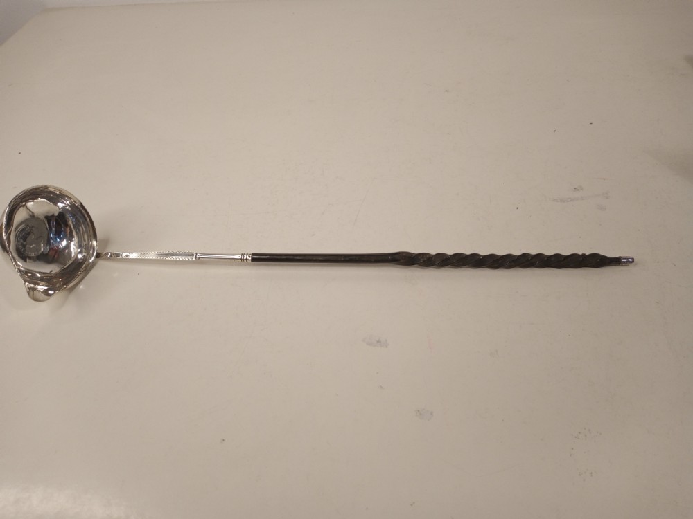 A mid-eighteenth century sterling silver punch ladle featuring a deep circular silver bowl and a long twisted dark handle.
