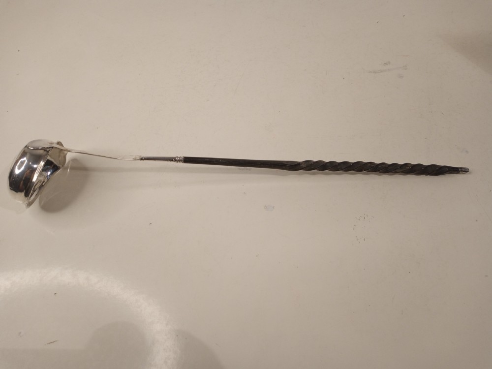 A mid-eighteenth century sterling silver punch ladle featuring a deep circular silver bowl and a long twisted dark handle. View II