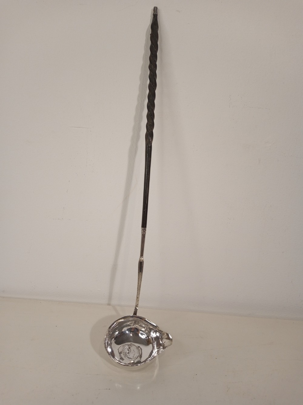 A mid-eighteenth century sterling silver punch ladle featuring a deep circular silver bowl and a long twisted dark handle. View IX