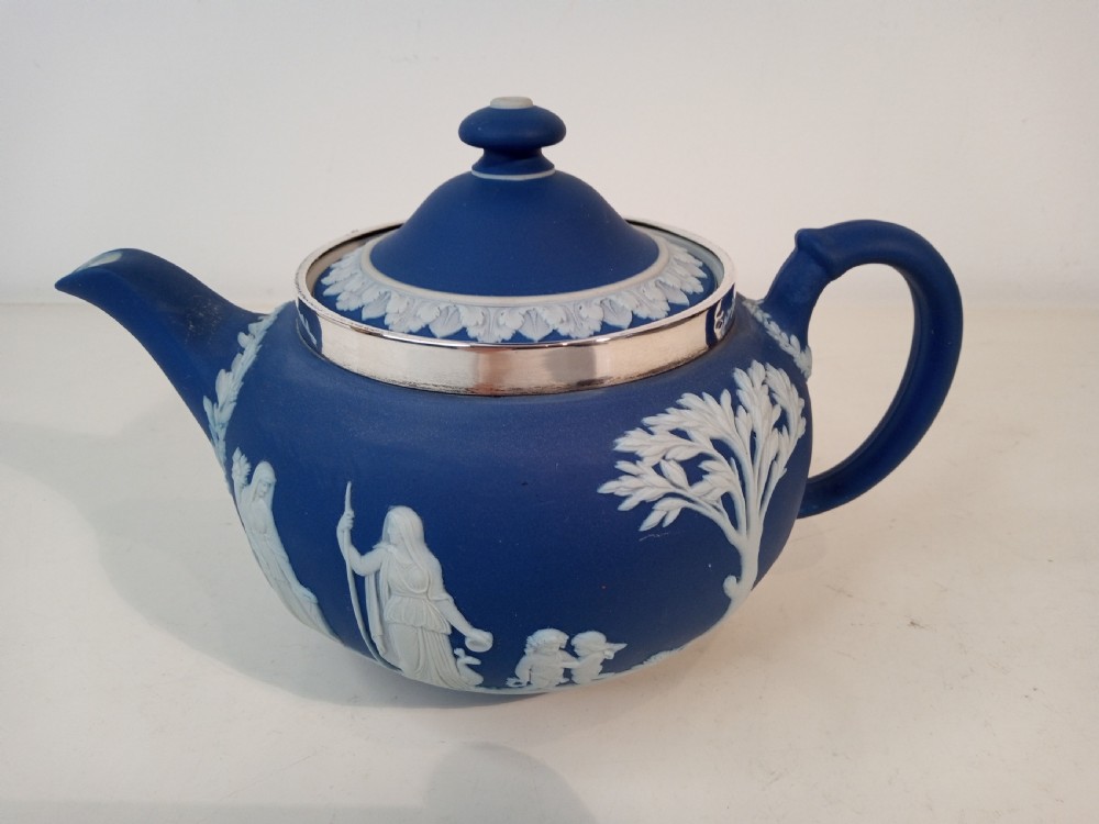 A blue stoneware teapot featuring white neoclassical bas-relief figures and a silver collar around the rim.